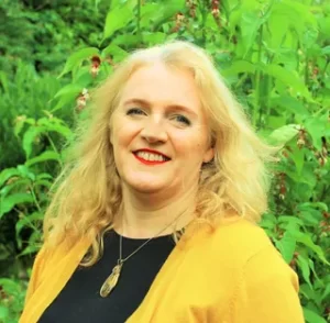 Colour photograph of Siobhan Stevenson, Director of Conservation Legacy. Siobhan has blond wavy hair and is wearing a black top and yellow cardigan